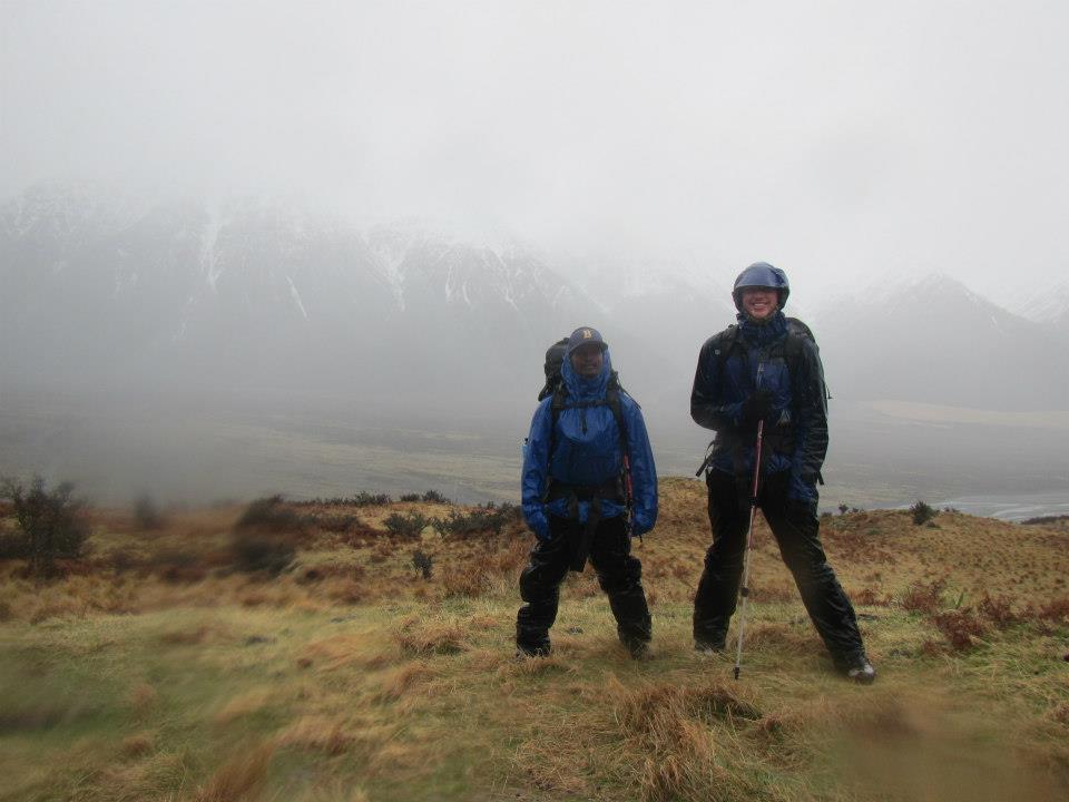 Two NOLS students wearing rain gear smile on a foggy, wet day in New Zealand's mountains