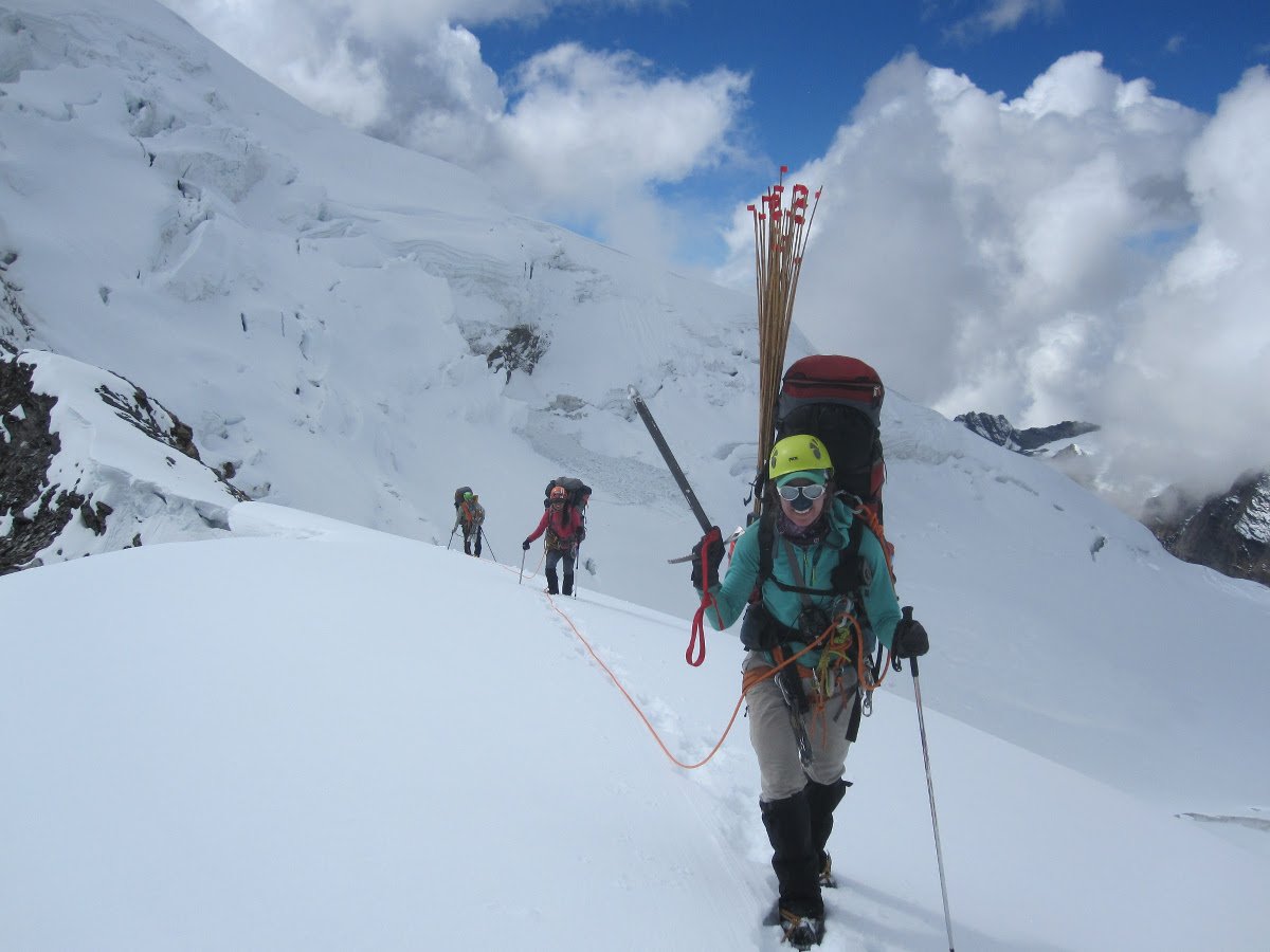 three people on a rope team hike across a snowy glacier in the Himalayas
