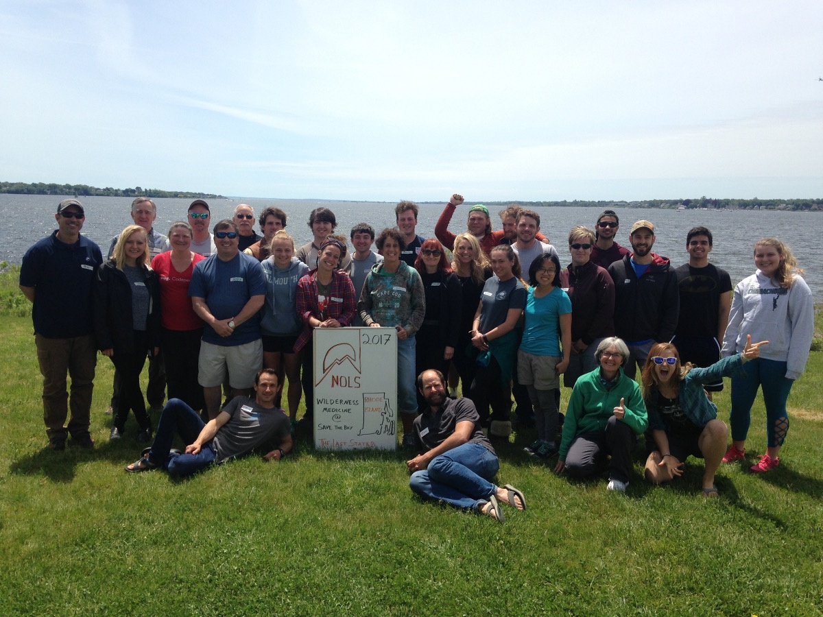 smiling students at NOLS' first wilderness medicine course in RI  pose for a group shot with the Narragansett Bay in the background