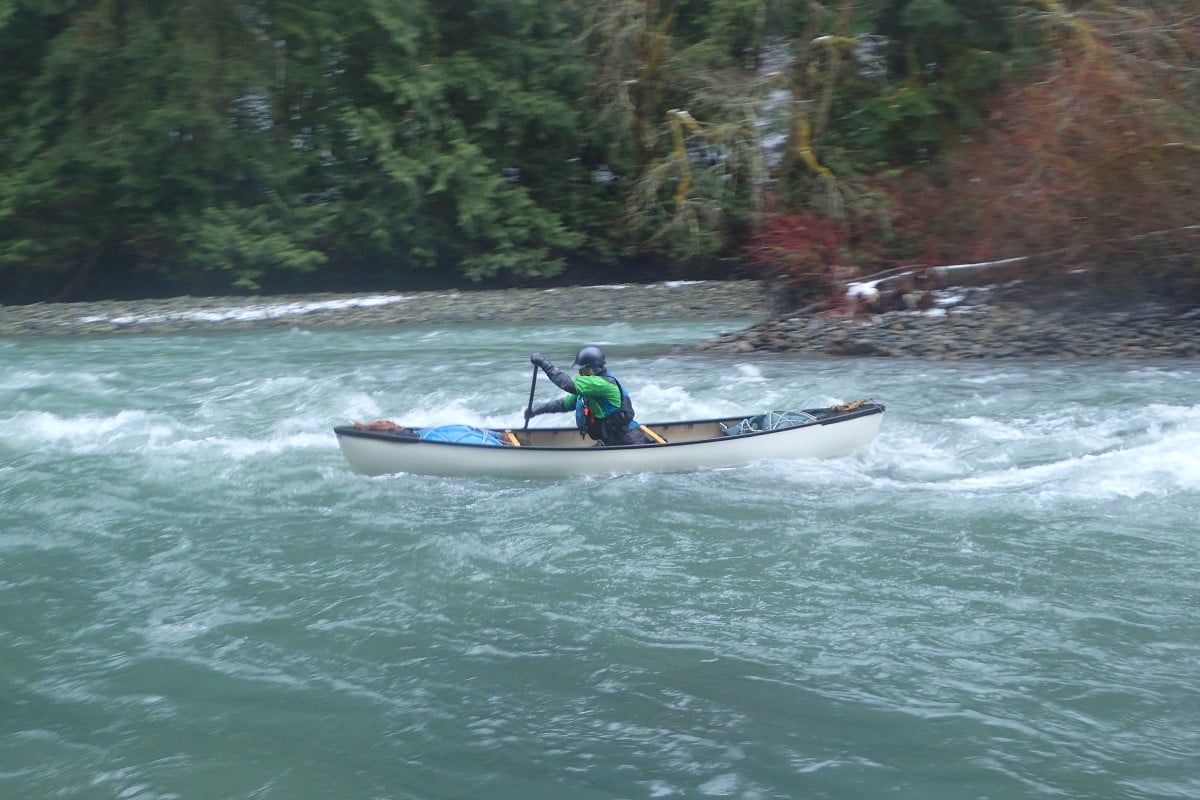 Lone paddler navigates a canoe through a whitewater rapid