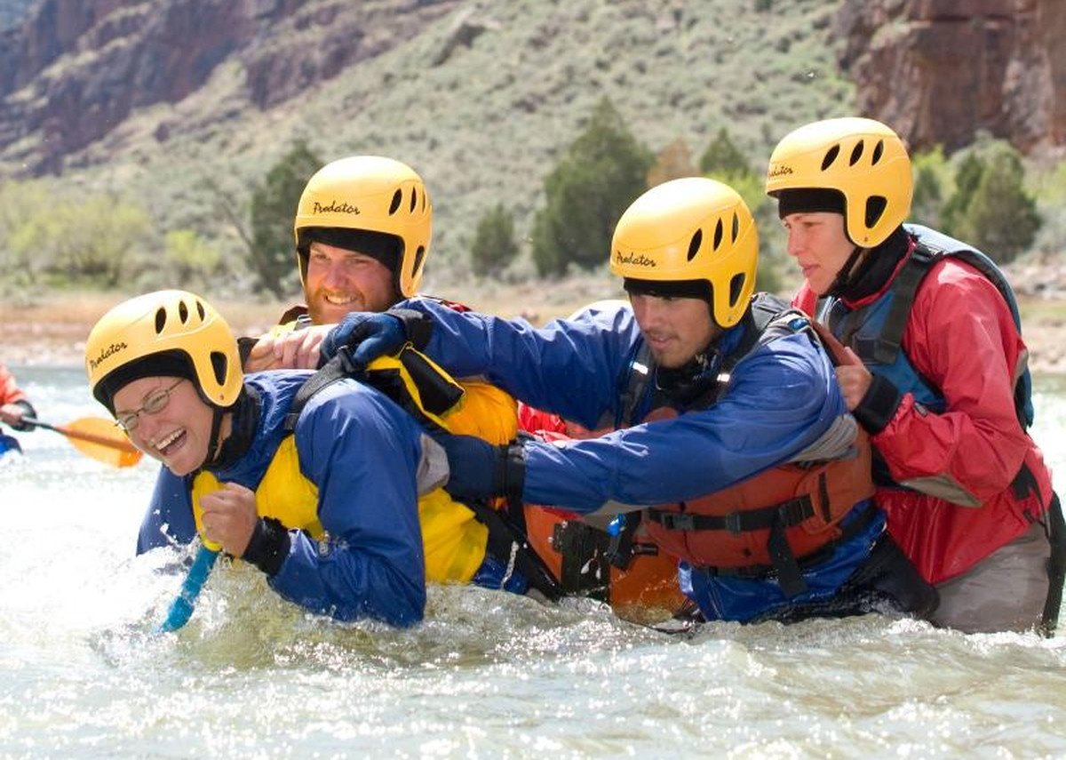 Four students wearing life preservers and helmets hold onto each other while practicing river rescue