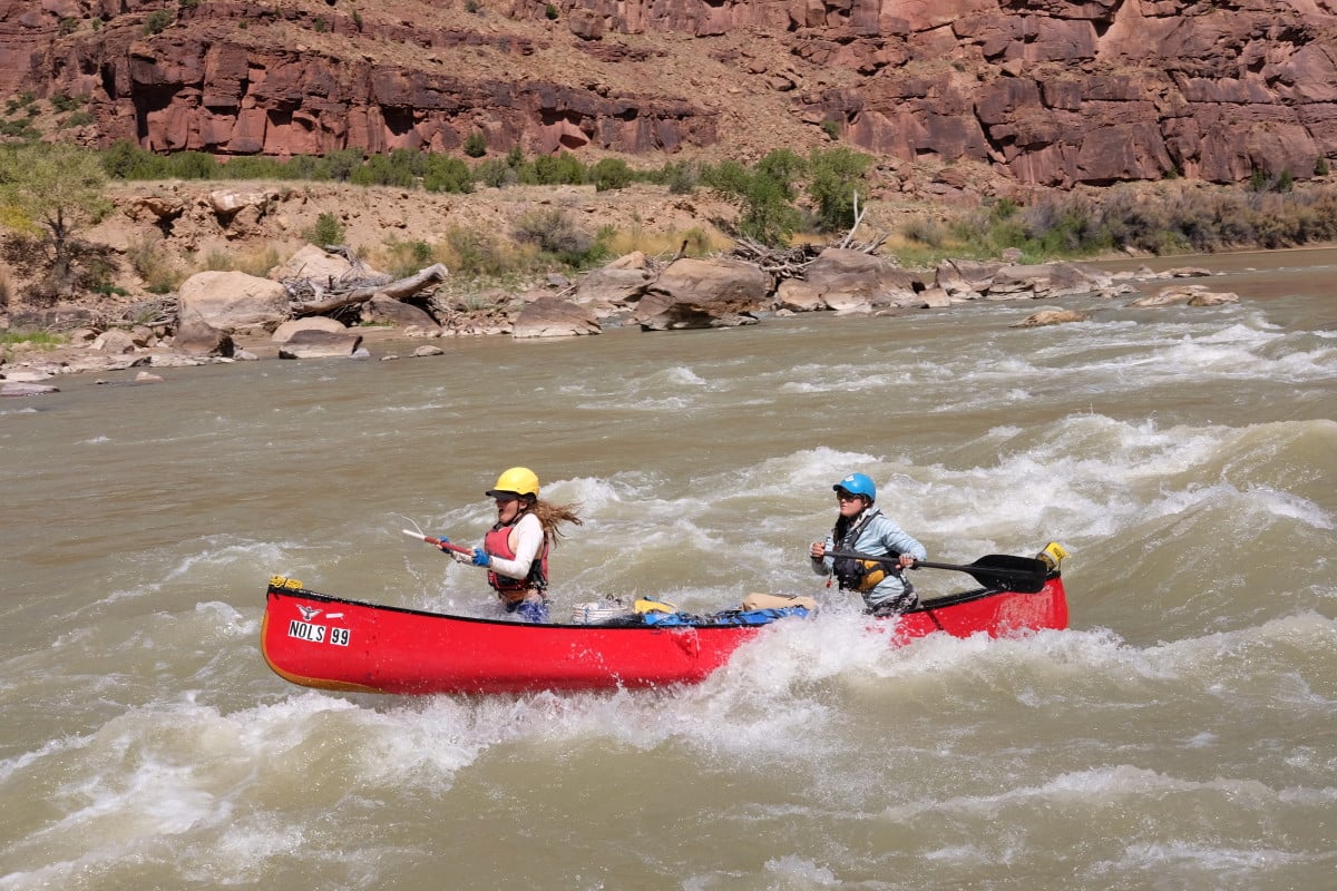 Two people paddle a red canoe in whitewater in a desert canyon