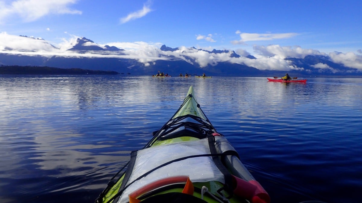 Sea kayak with other group members and mountains in the background