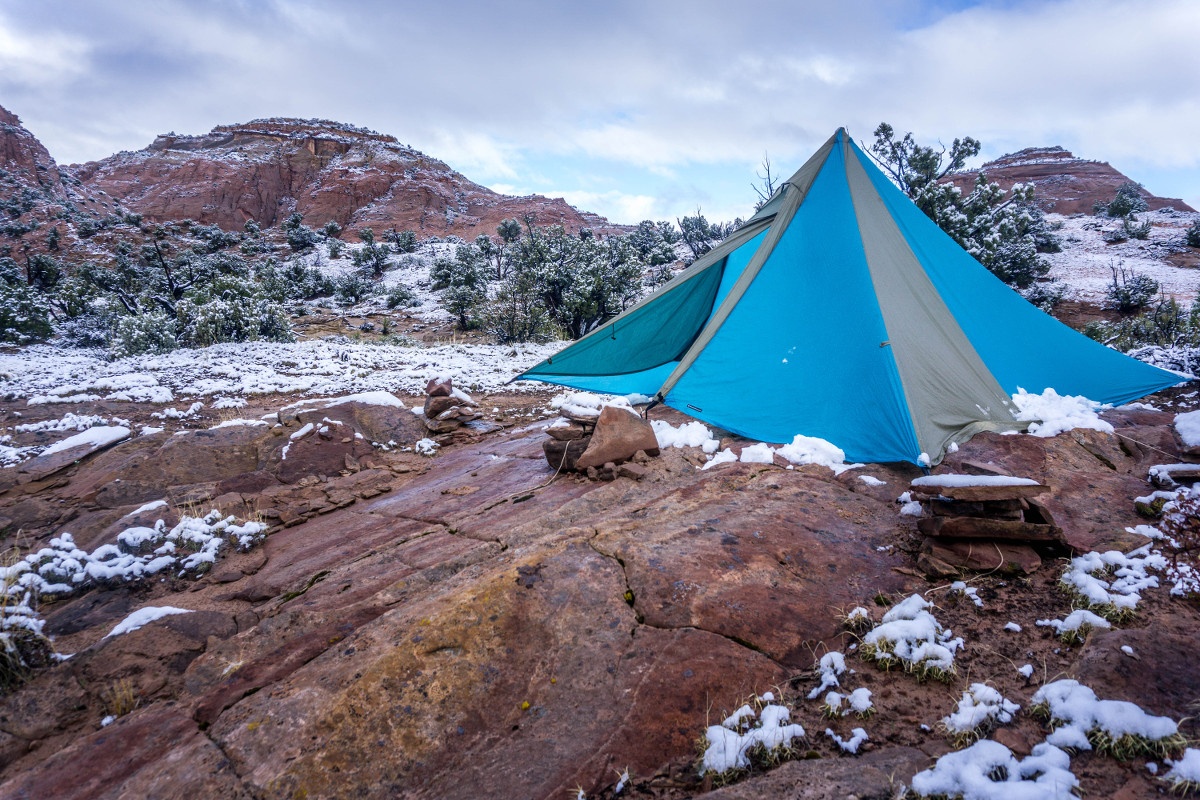Blue and tan mega mid tent pitched on red rock with patchy snow