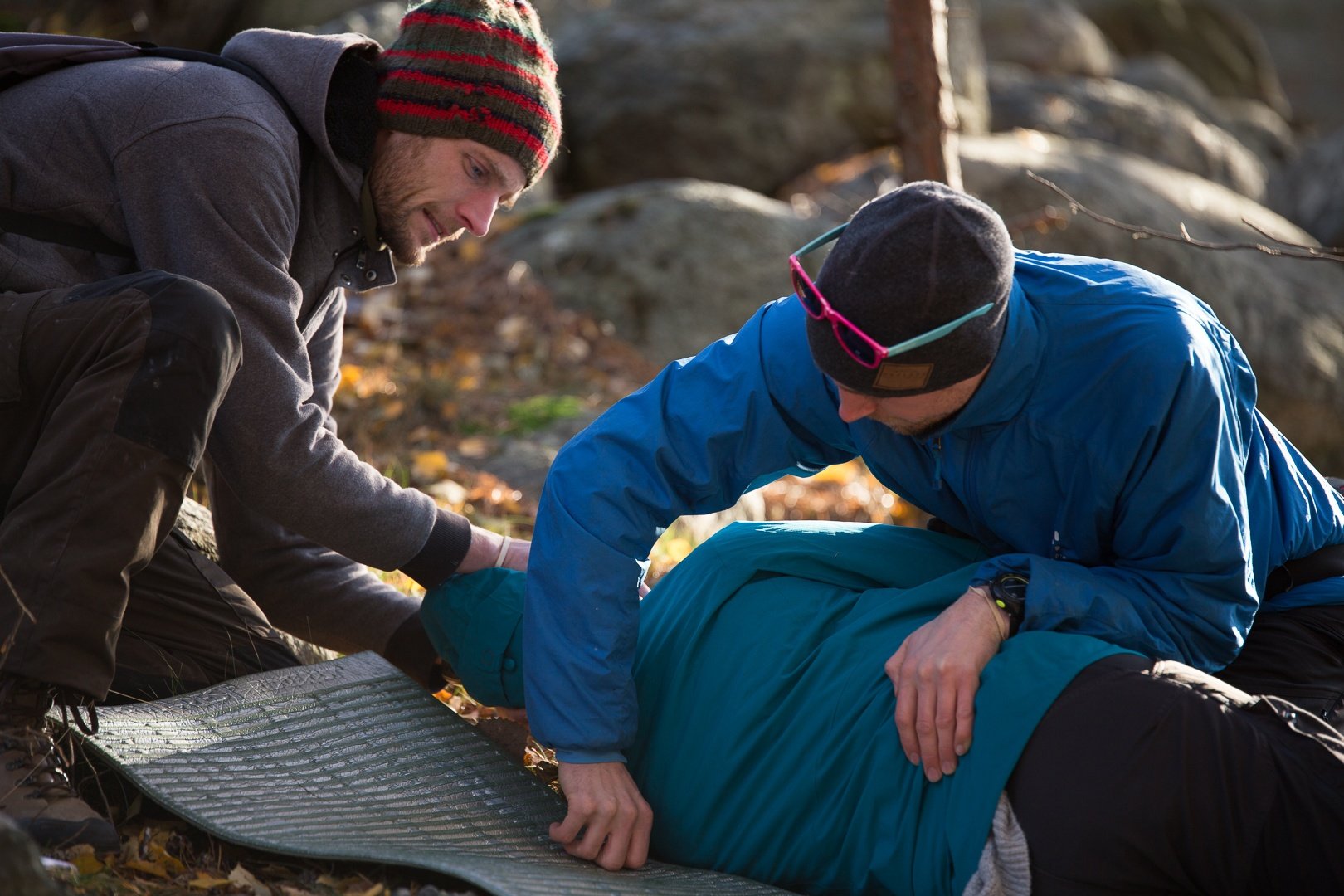 two NOLS Wilderness Medicine students care for a patient lying on his side on a camp pad