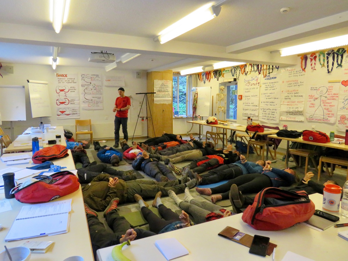 NOLS Wilderness Medicine students line on their backs on the floor of a classroom surrounded by desks