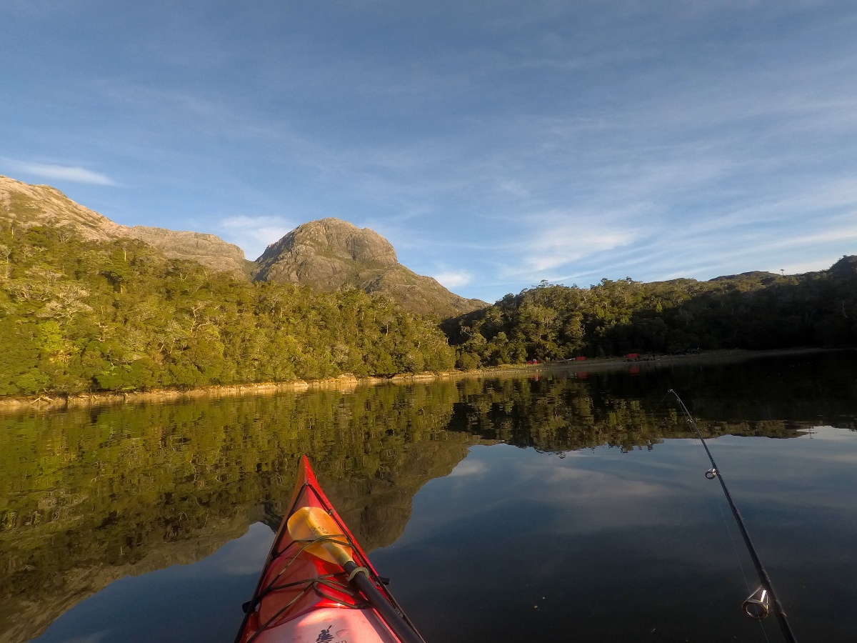 Picture taken from a sea kayak with a fishing rod and hills in the background
