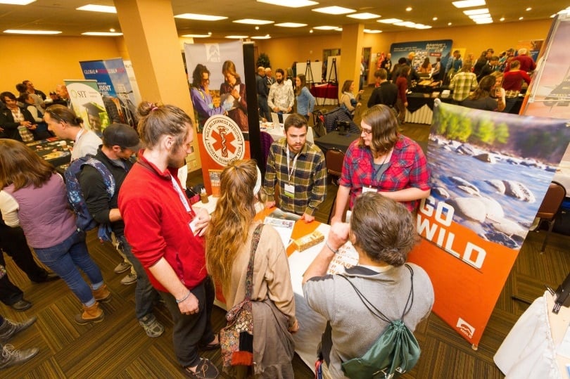 Group of people standing around a table talking with NOLS posters in the background at the 2017 WRMC