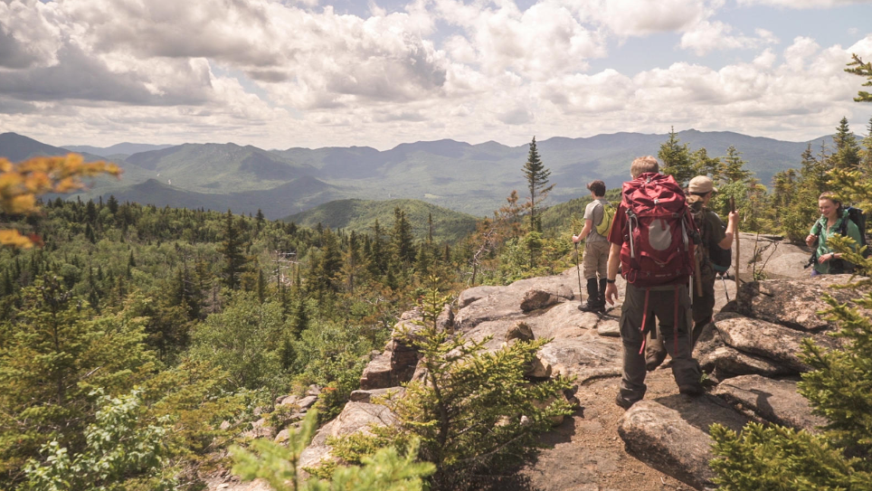 A group of four teenagers backpacking stop on a ridge overlooking rolling green mountains