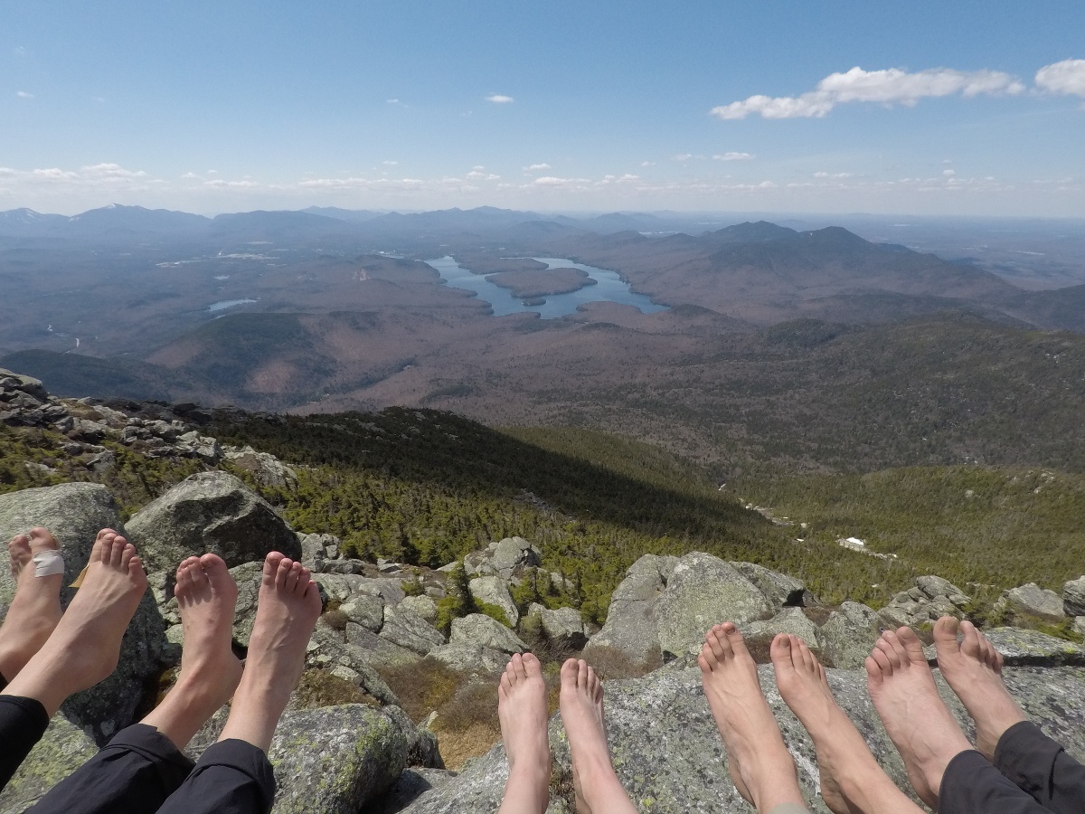 Five sets of soggy feet getting some sunshine at the top of a rocky slope looking down on a lake and forest