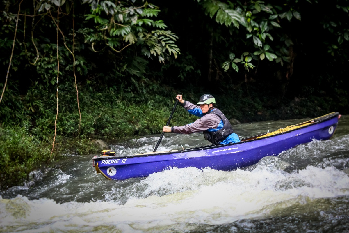 Woman paddles a purplish blue canoe through whitewater in Costa Rica