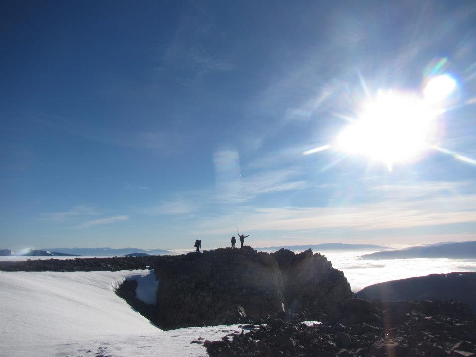 Three distant silhouetted figures on a ridge surrounded by snow on a sunny day