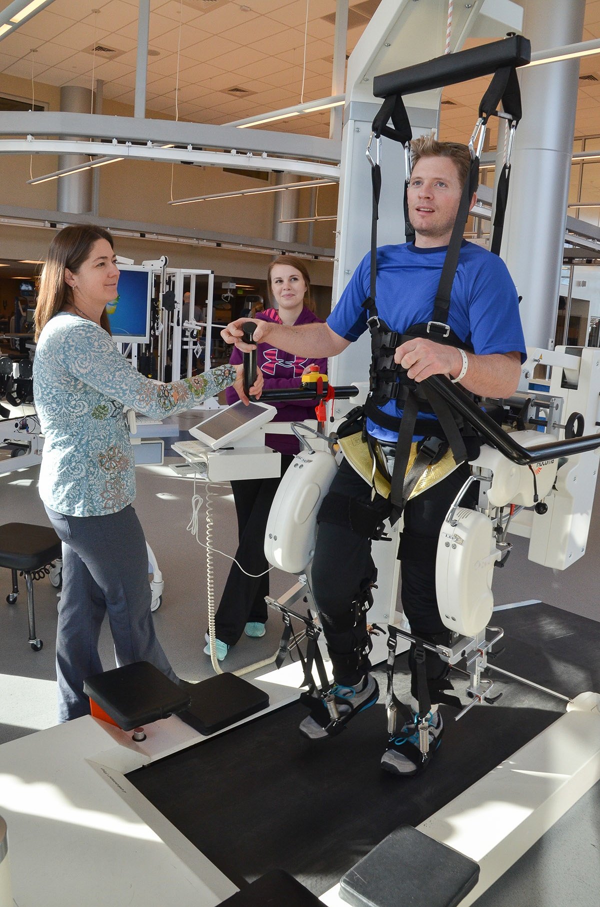 Jim Harris works with two physical therapists while strapped into an exercise machine 