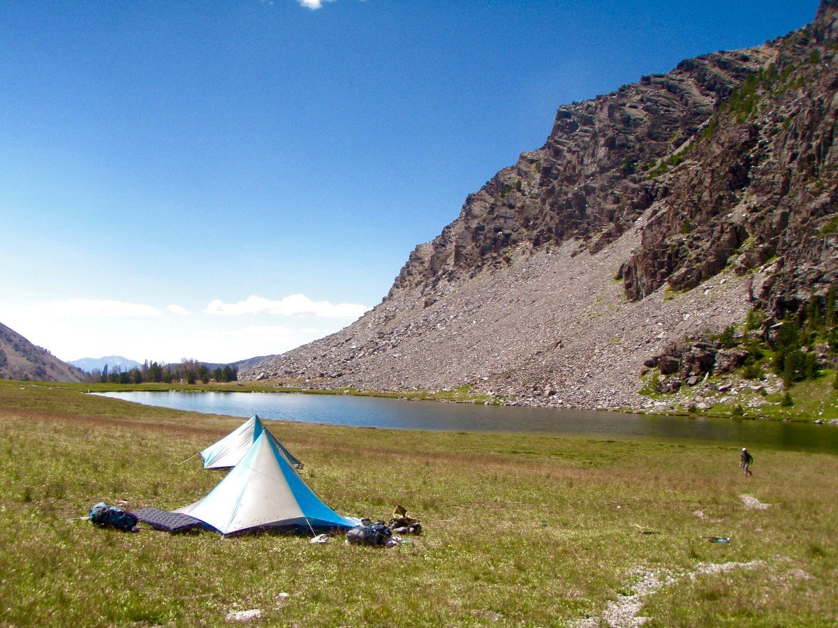 blue and tan mega mid tents set up on grass near a glassy alpine lake