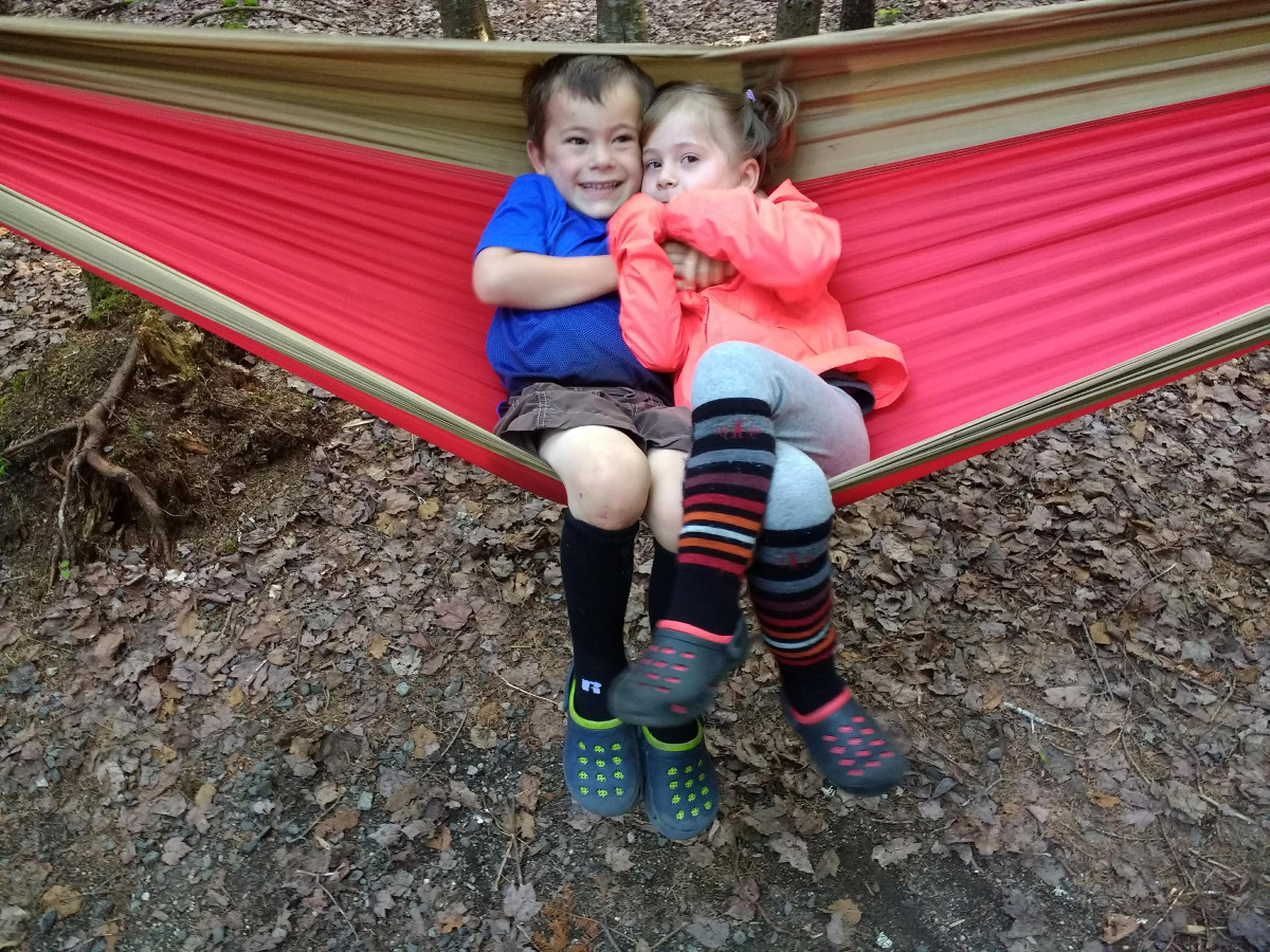 two smiling children sit together in a red and tan hammock while camping