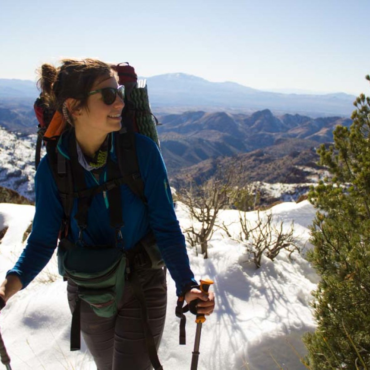 Smiling woman wearing backpack and holding trekking poles standing in the snow in the Southwest