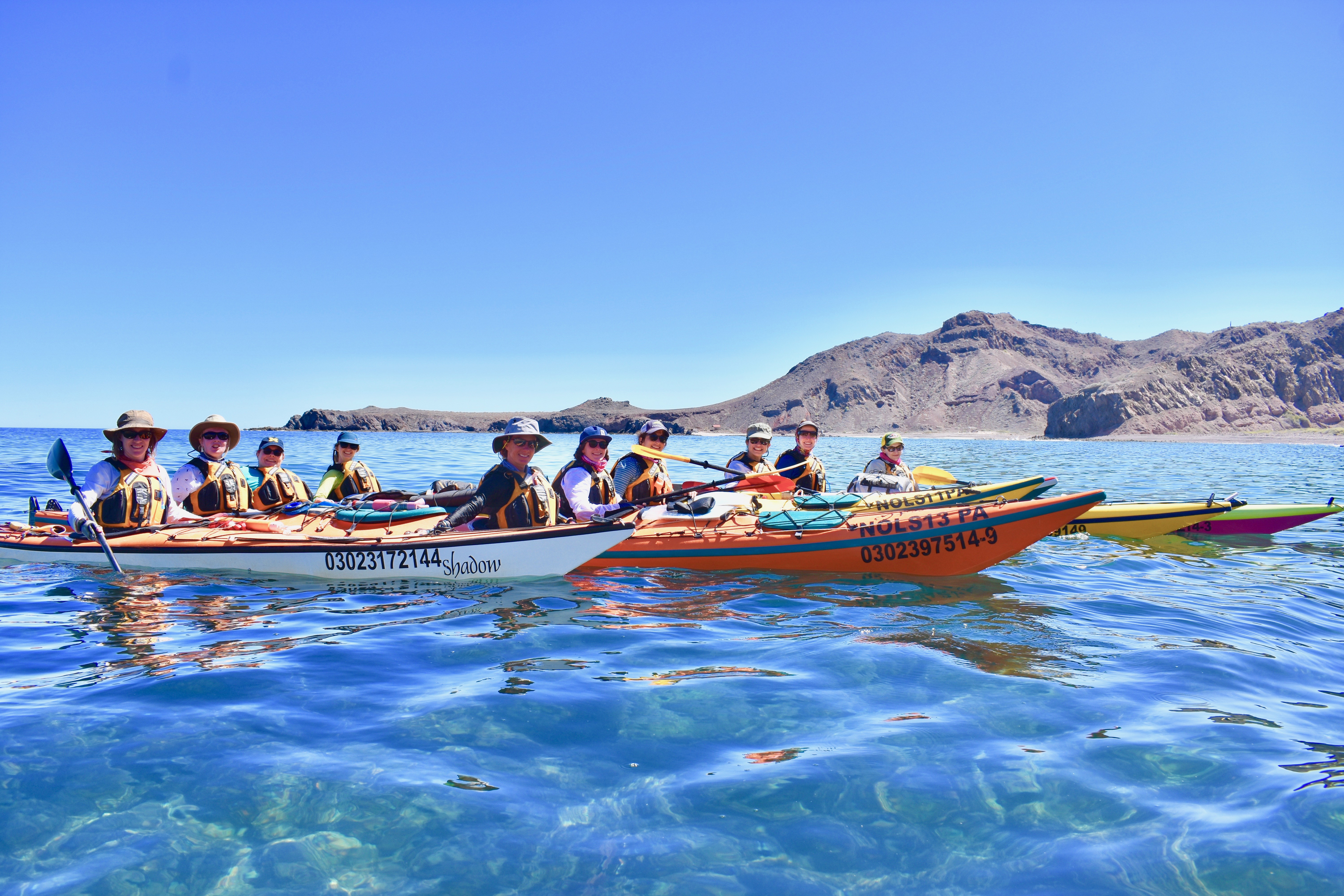 Women wearing sun hats and life preservers in colorful kayaks on clear water in Baja