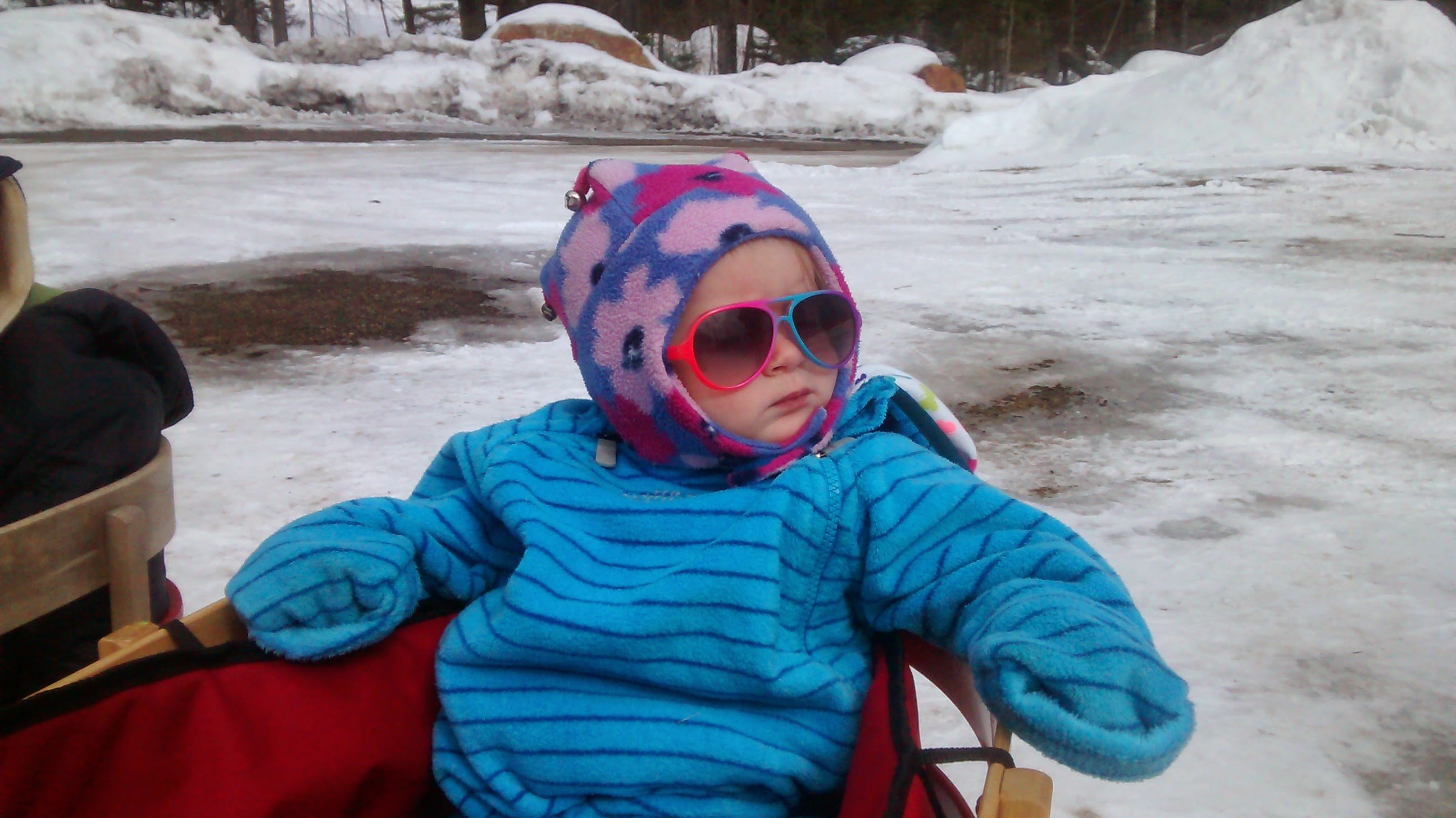 toddler in winter apparel with snow in the background and wearing sunglasses