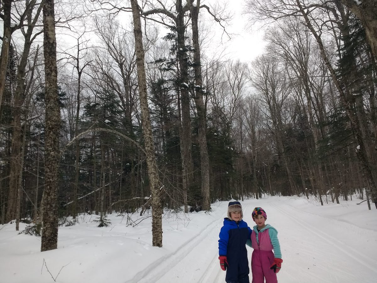Two children smile for a photo while cross country skiing