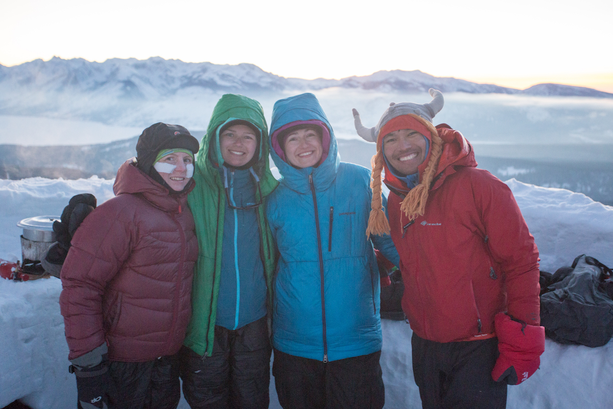 Four happy people smile in winter clothing with one wearing a fun hat