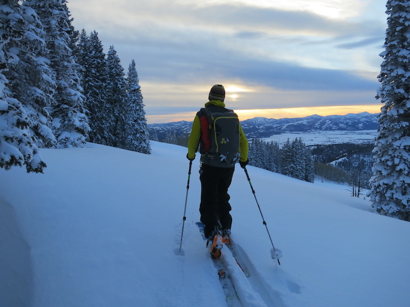 NOLS participant backcountry skis as the sun sets over snowy mountains