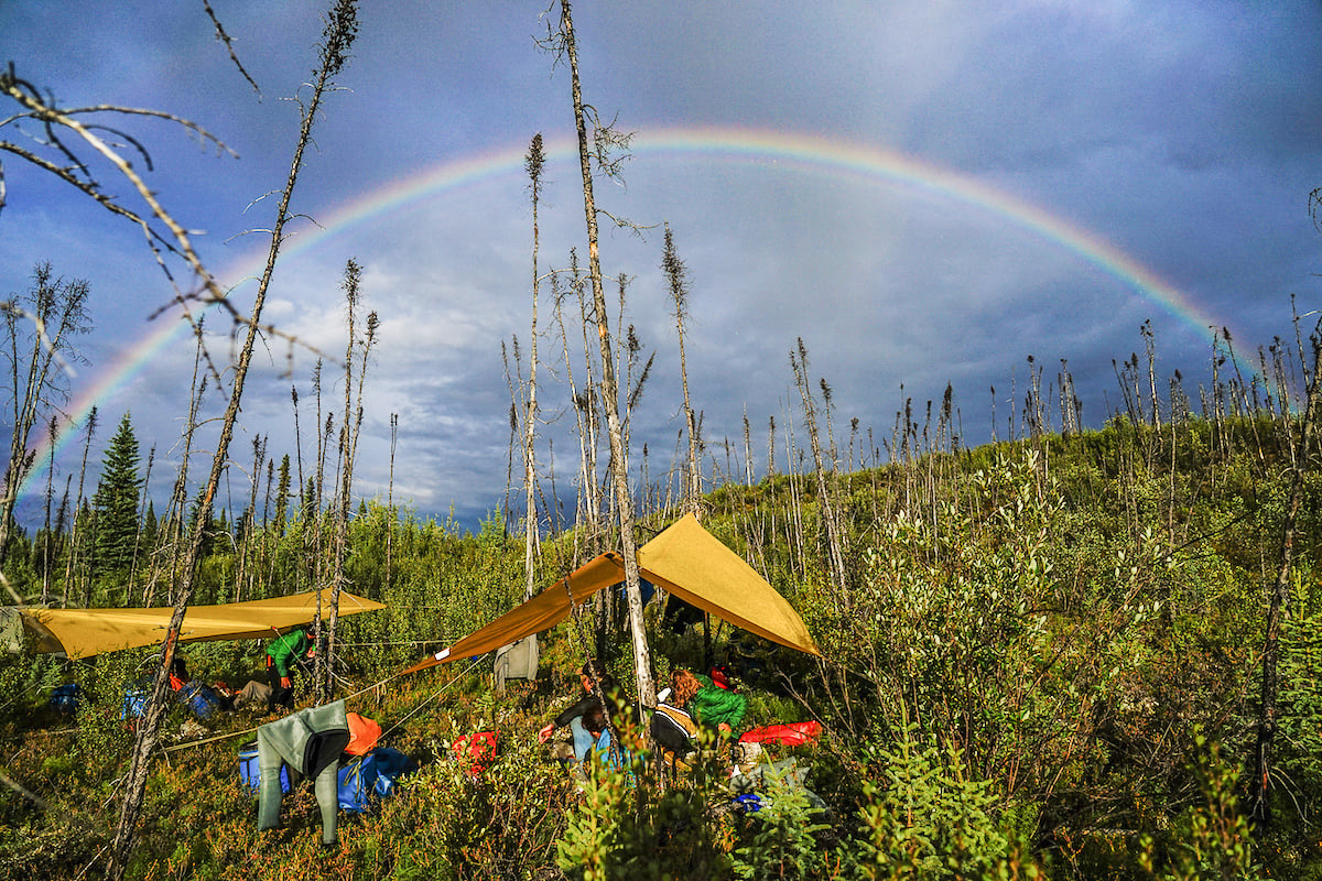 rainbow above a campsite in the Yukon with tarps and clothes hung out to dry