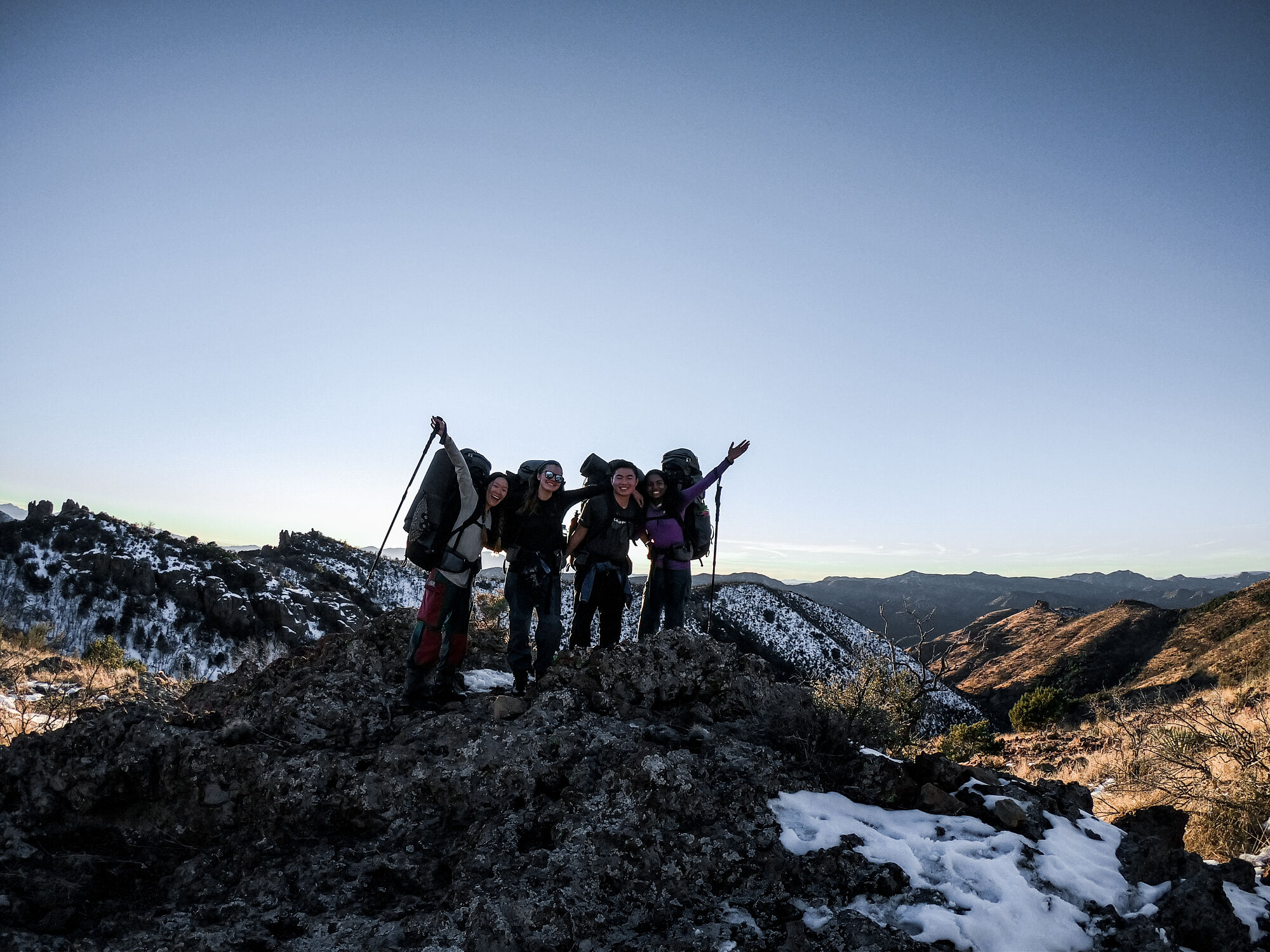 Business school students on a NOLS expedition smile for a photo on top of a snowy mound