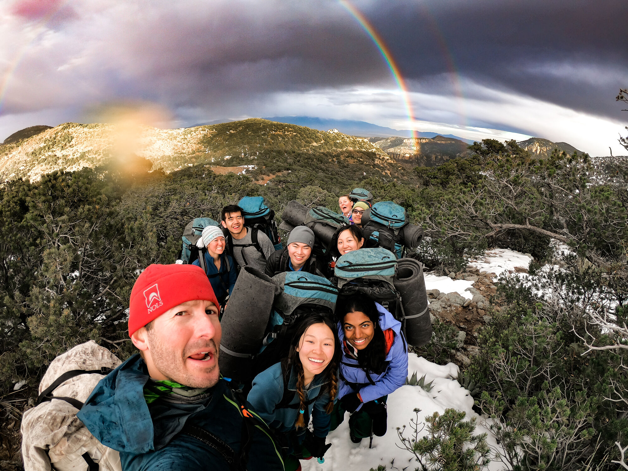 Selfie shot of a group of smiling backpackers with a rainbow in the background