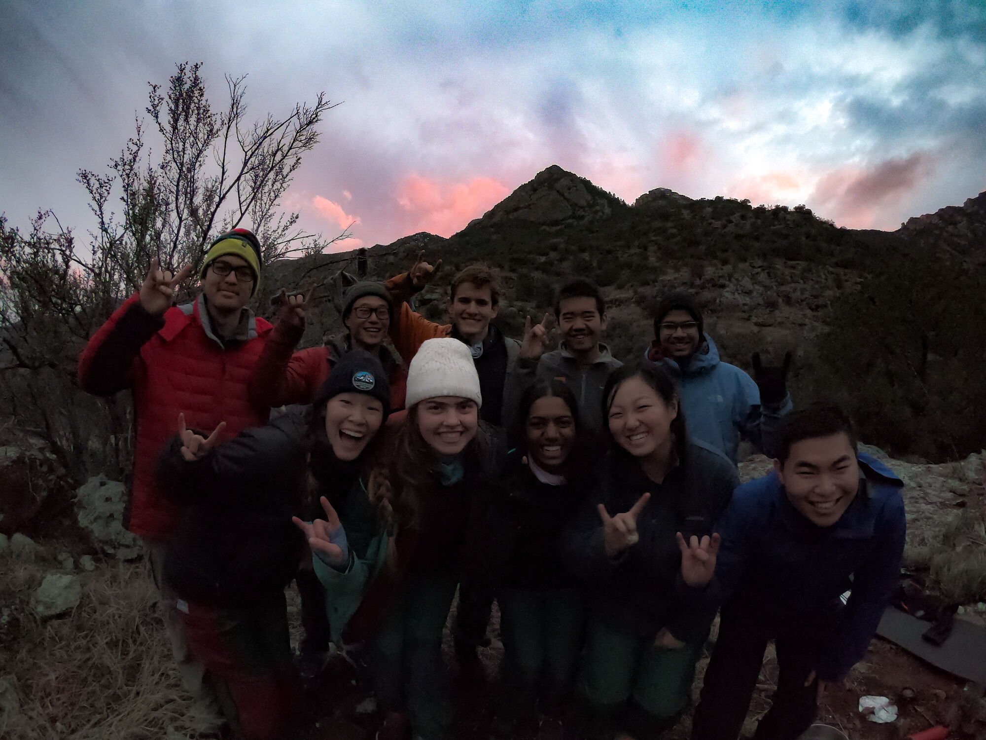 A group of business school students on a NOLS expedition hold up hand signals while the sun sets behind them