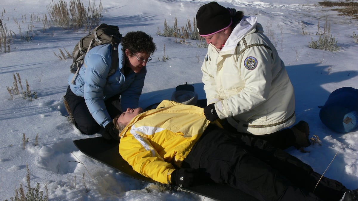 two NOLS Wilderness Medicine students kneel beside a patient in the snow and perform a mock initial assessment