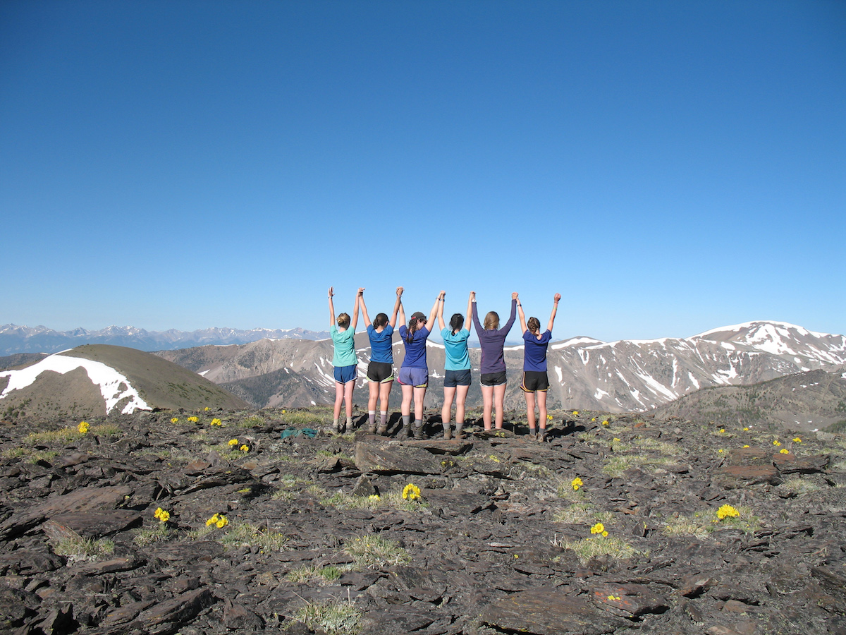 six teenage girls raise arms in celebration while backpacking in the Pacific Northwest