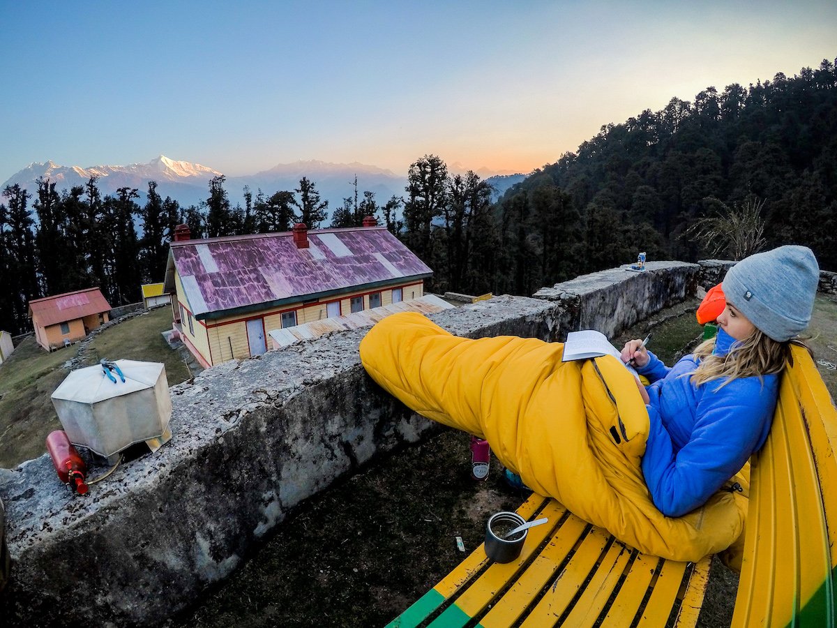 NOLS student wrapped in a sleeping bag sits on a bench journaling in the Himalaya