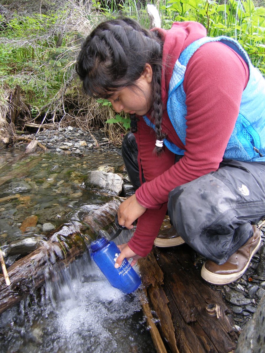 Hiker filling up water bottle from a stream
