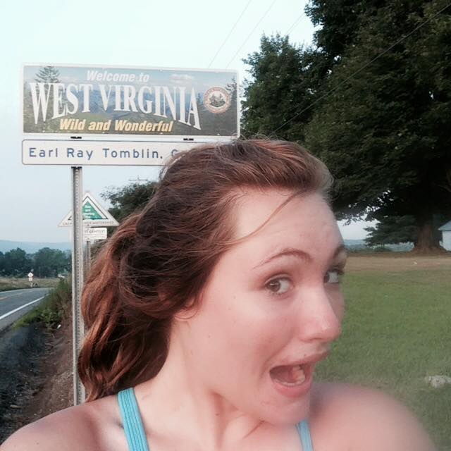Selfie of female runner in front of the Welcome to West Virginia sign and a group of trees
