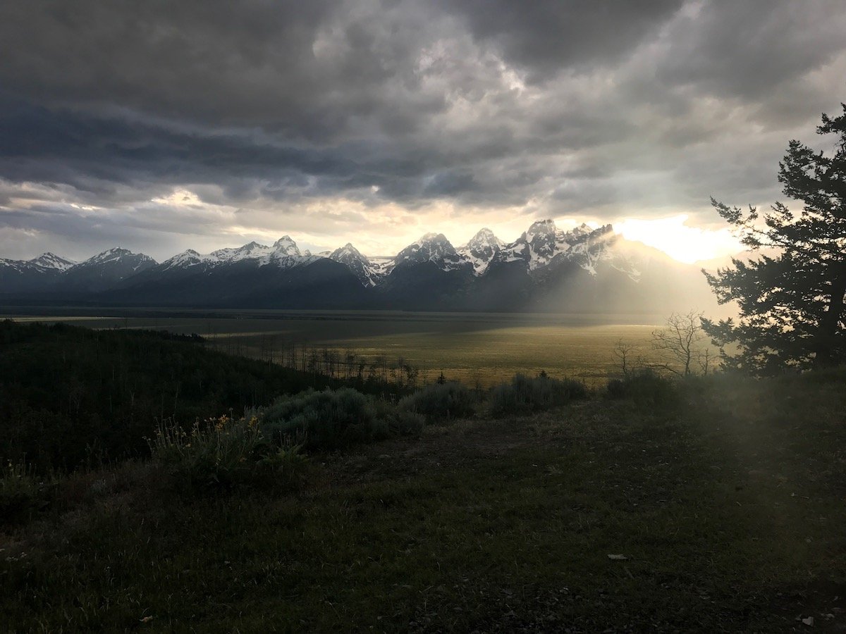 view of the snow-capped Tetons with sunlight shining through dramatic clouds