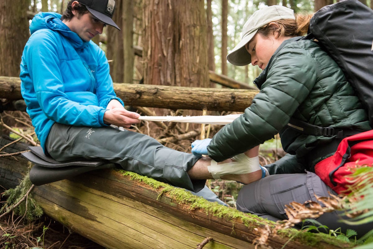 wilderness medicine student practices taping an ankle of a mock patient sitting on a log