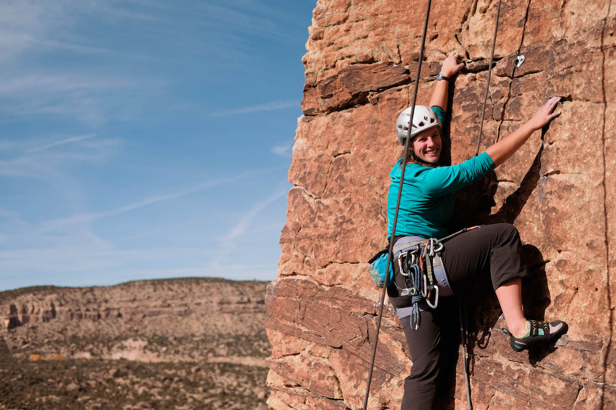 smiling NOLS student climbing on reddish rock