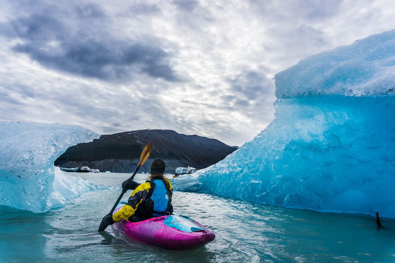 Kayaker in a pink boat paddles past crystal blue icebergs