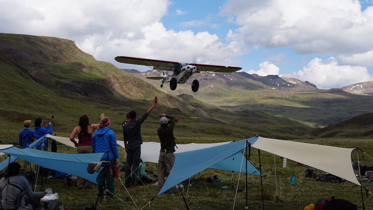 NOLS students stand in camp waving to a bush plane in the mountains of Alaska