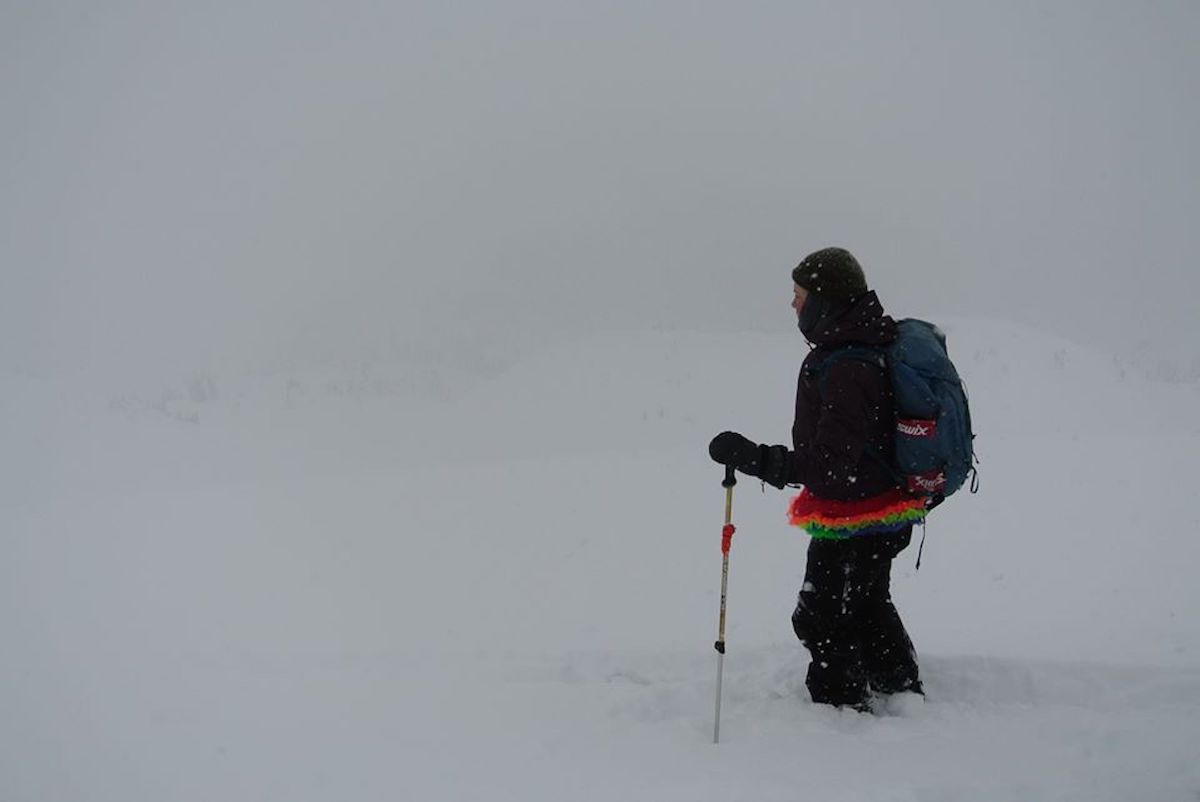 the author in a snowstorm standing on backcountry skis with a rainbow shirt sticking out from under her winter gear