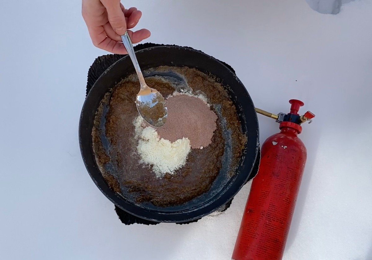 using a spoon to stir cocoa and powdered milk into no-bake cookie batter on a campstove