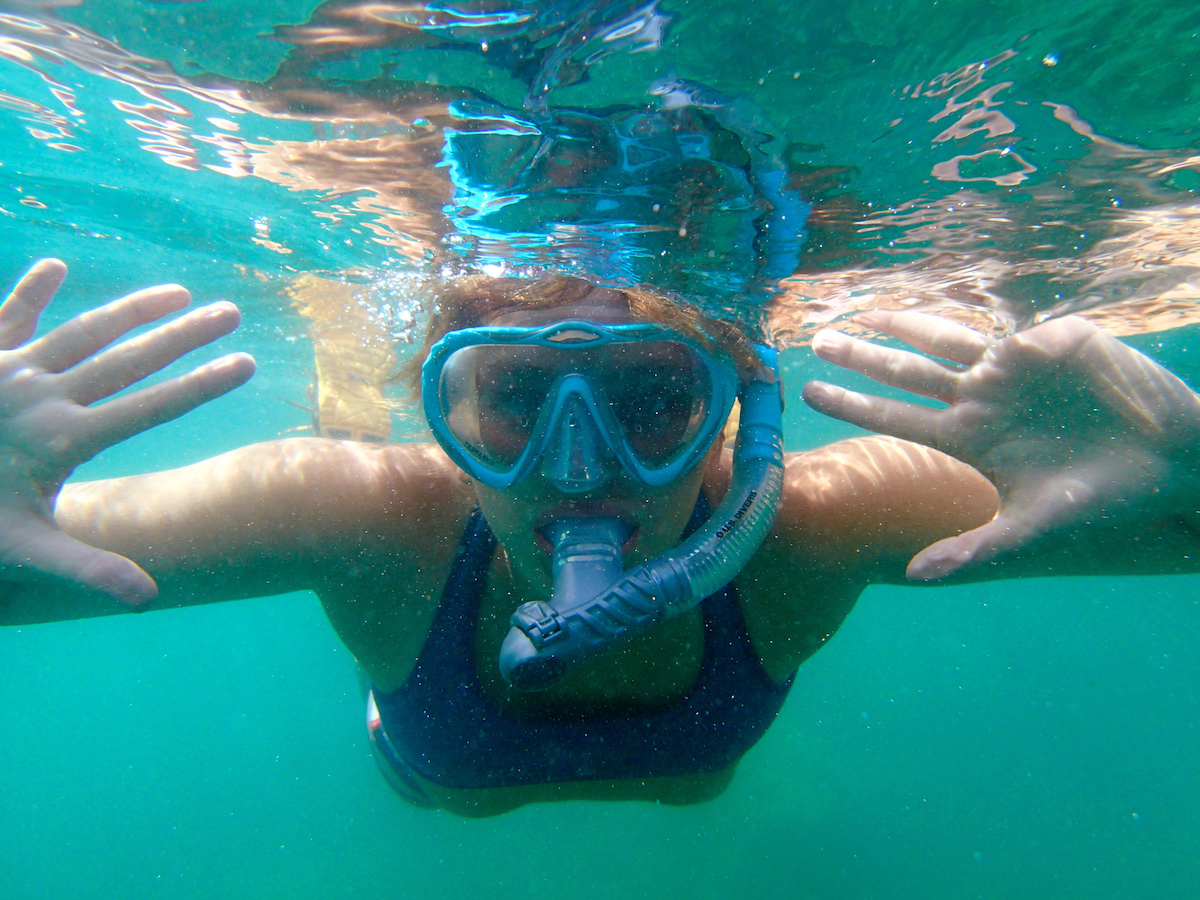 girl wearing purple top holds hands out while swimming underwater with a snorkel