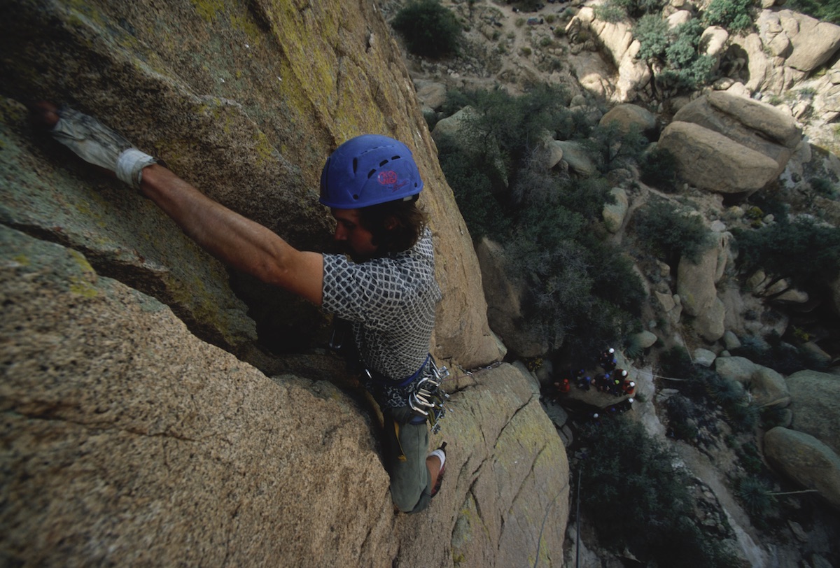 NOLS student wearing blue helmet rock climbs in the Southwest with cluster of teammates far below