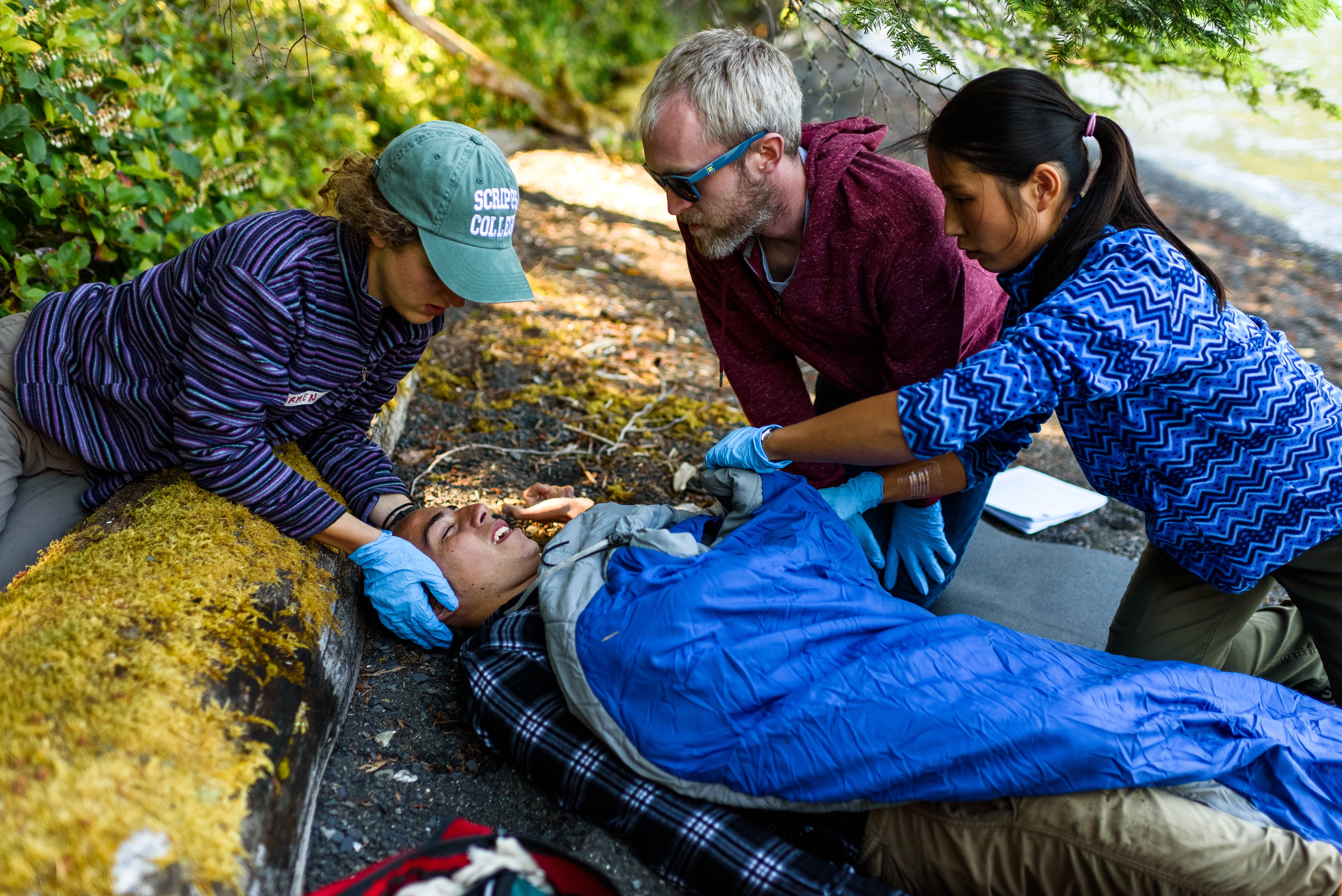 three NOLS students practice caring for a patient in a sleeping bag