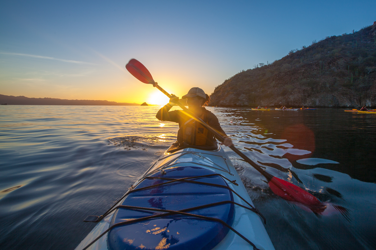 NOLS student paddles kayak in Baja with sun setting over calm water