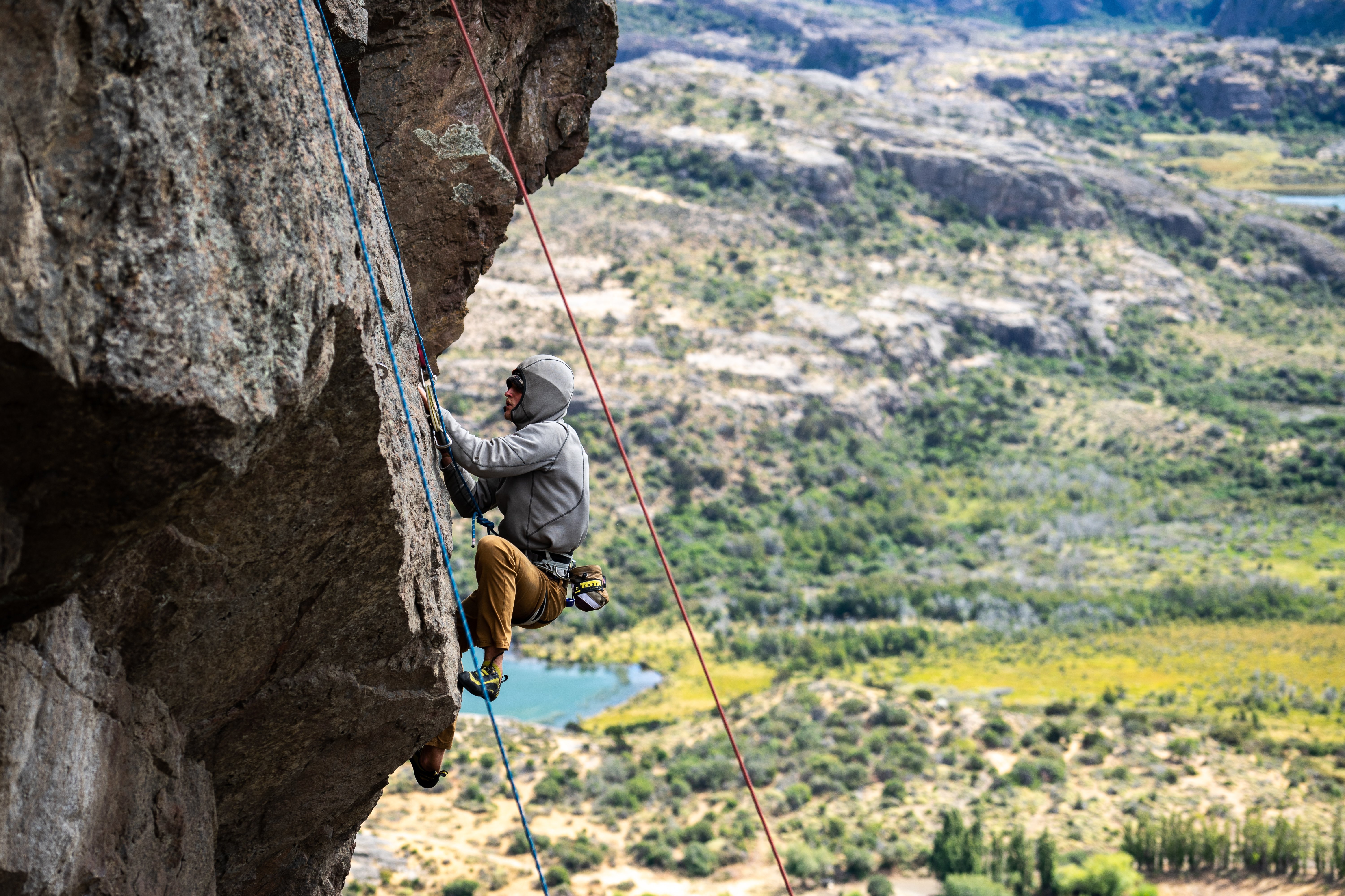rock climber on a rock face high above a blue lake and lush valley in the mountains