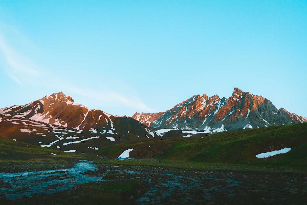 braided stream in a green valley in Alaska surrounded by rocky peaks with snow patches