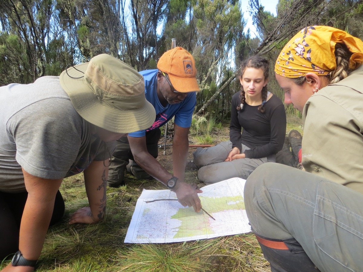 NOLS instructor teaches students how to read a topo map spread out on the ground in Tanzania