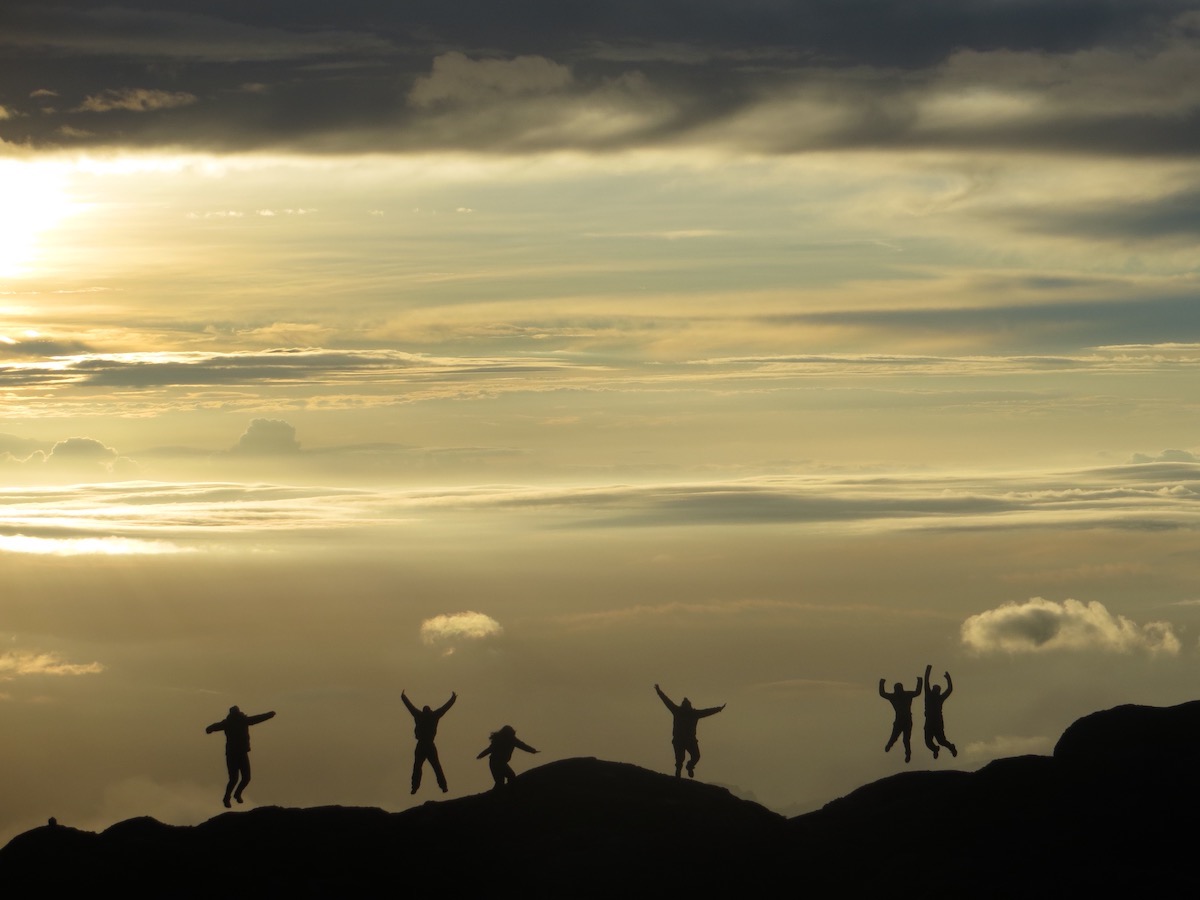 five silhouetted figures leap into the air on the top of a peak in Tanzania