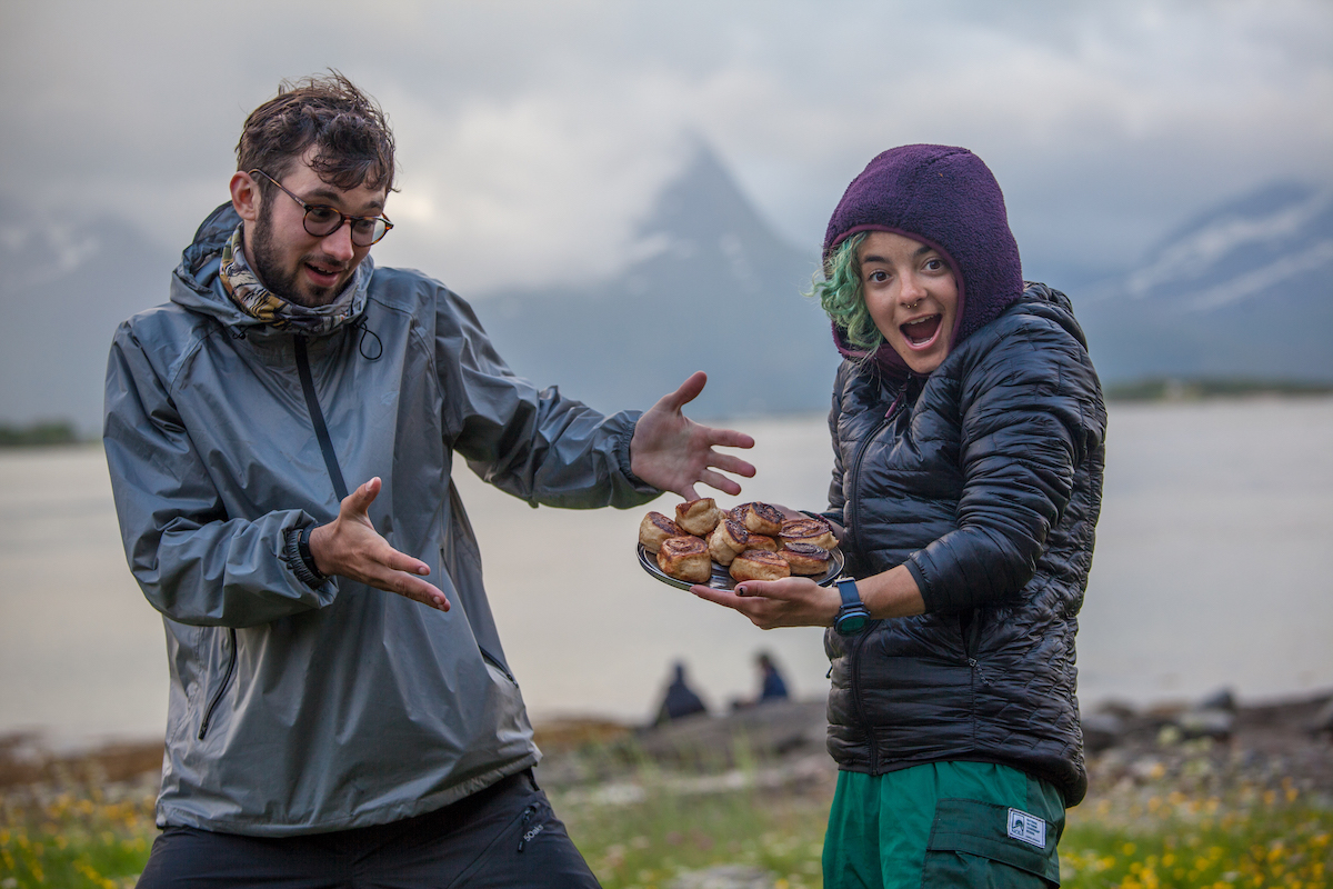 two people make goofy faces and show off a pan of cinnamon rolls in Scandinavia on a foggy morning